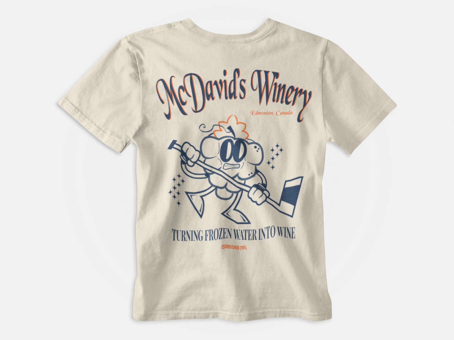 back of shirt, cream colored, blue and orange lettering, grape holding a hockey stick, turning frozen water into wine, mcdavid's winery, edmonton oilers, connor mcdavid